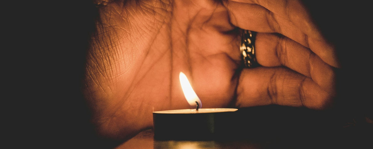 Aansteker voor ouderen: een oudere hand met een ring schermt een brandend waxinelichtje af